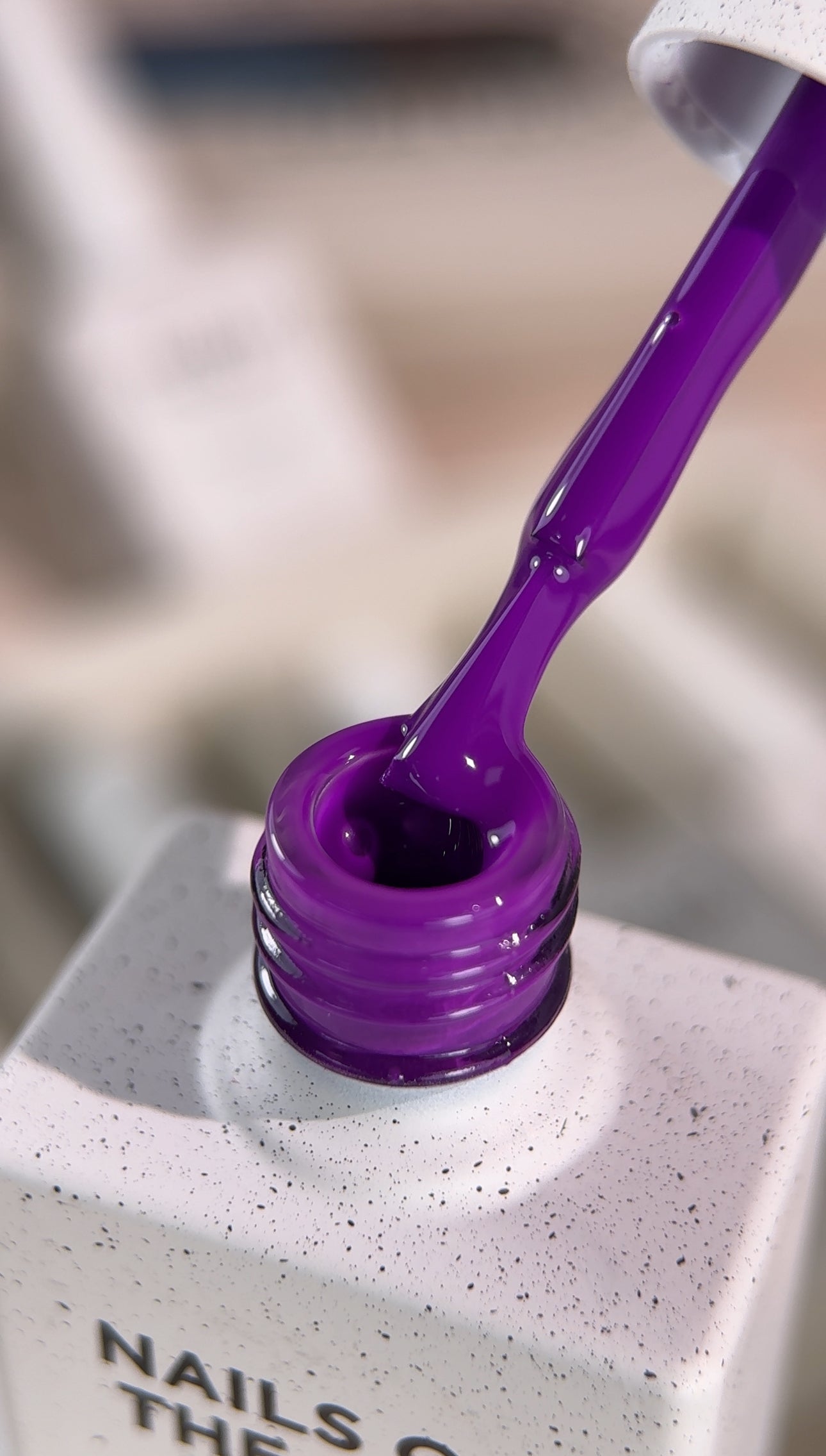 Close-up of a purple nail polish bottle with a brush on a speckled surface.